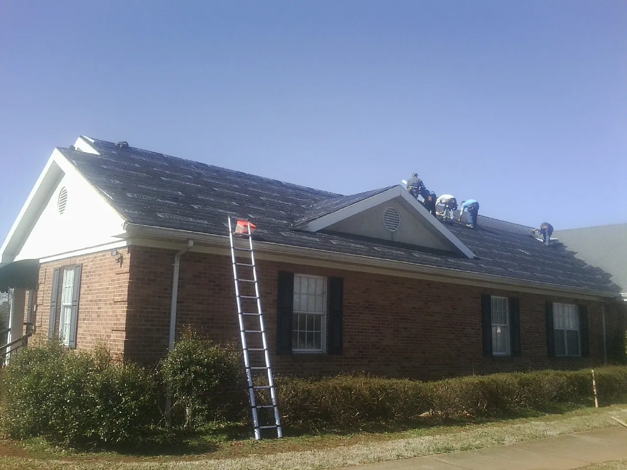Crew tearing shingles off a brick ranch roof with a ladder set — Emergency Roof Repair work by our crew in Wilder
