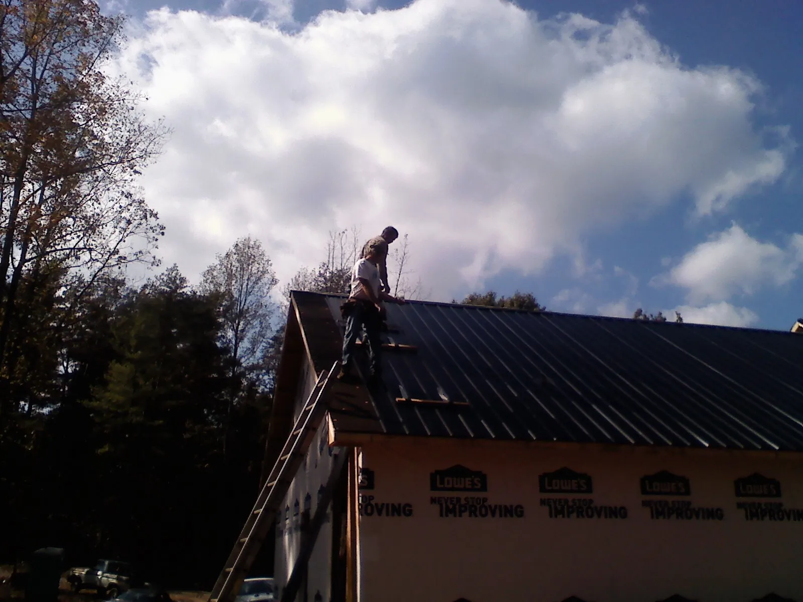 Roofer fastening dark metal panels high against a cloudy sky, from a Roof Inspection job in Wilder