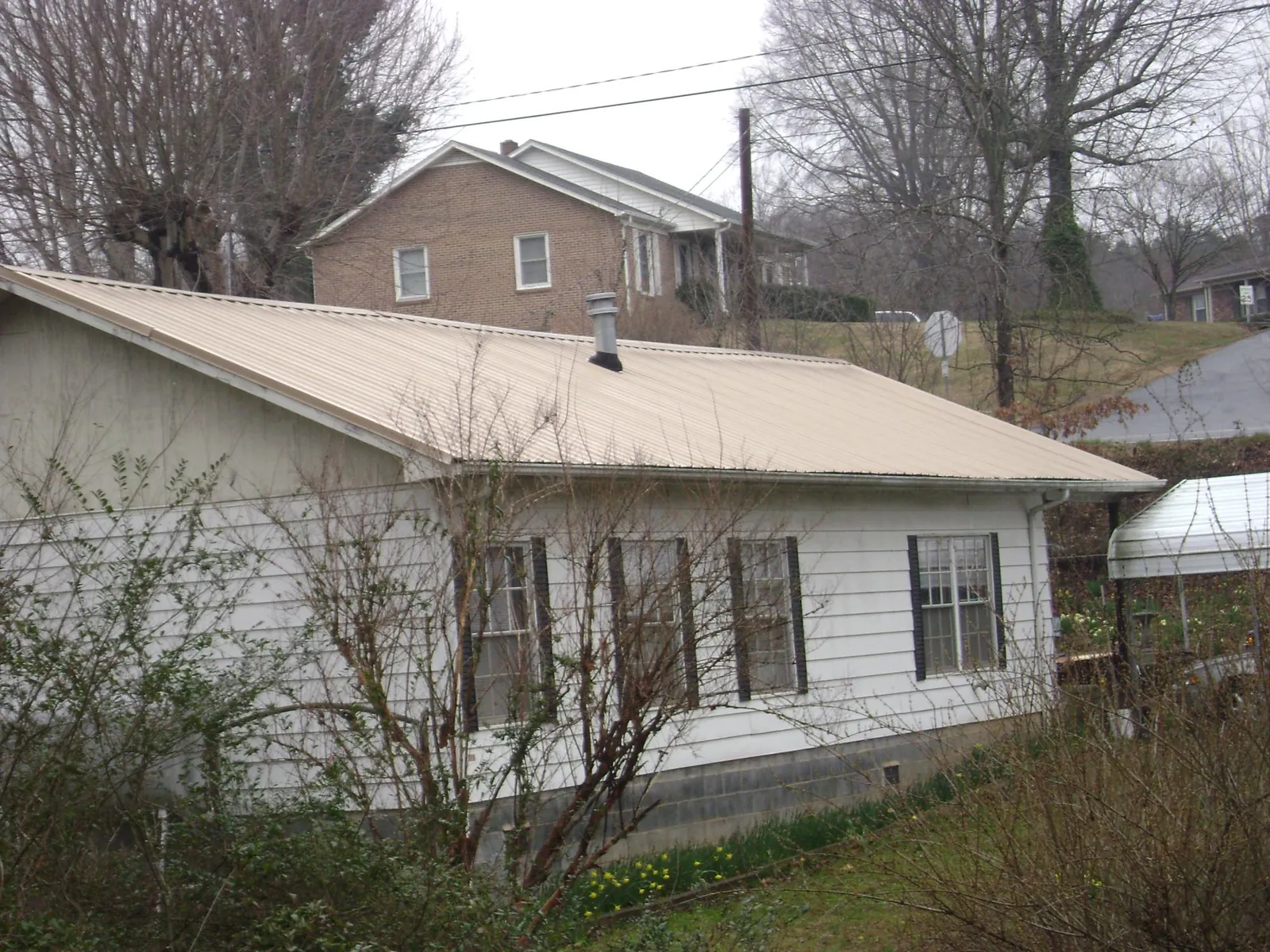 Tan metal roof on a white sided house set into a hillside — Commercial Roofing by Roofing Brothers in Wilder